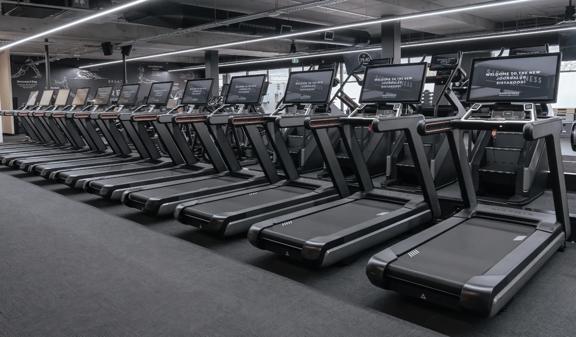 Row of Matrix Fitness treadmills with large digital screens, positioned in a modern gym.